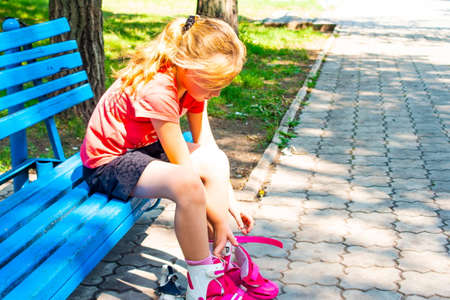 A blond girl dresses red rollers, sitting in a park on a blue bench.の写真素材