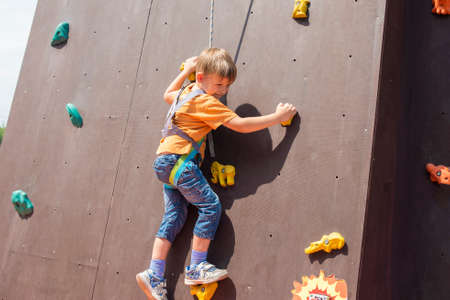 A frightened and happy little boy carrying an artificial rock with a safety rope, is engaged in rock climbingの写真素材
