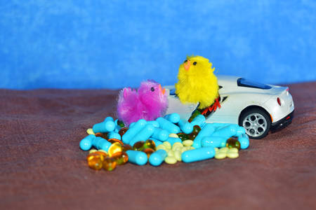 A toy car and different type of pills on a brown surface on a blue background. The concept of...
