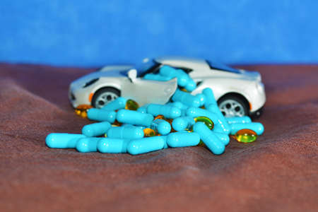 A toy car and different type of pills on a brown surface on a blue background. The concept of pharmacological industryの写真素材