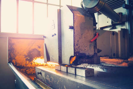 Metal parts on a flat grinder are treated with an abrasive wheel, sparks fly from under the circle,...