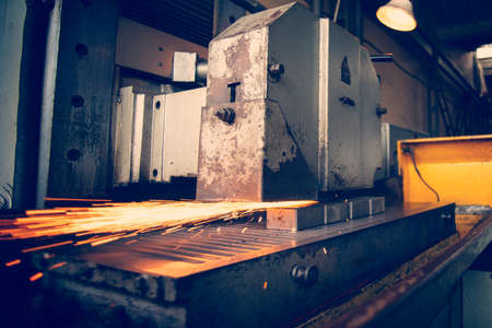 Metal parts on a flat grinder are treated with an abrasive wheel, sparks fly from under the circle,...
