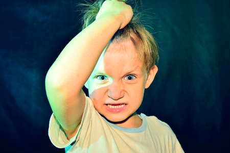 The evil boy tears his hair with a red-blue backlight on his head. Studio shootingの写真素材