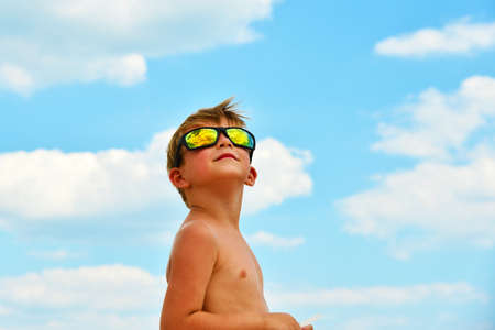 A little boy looks at the cloudy sky with glasses. The clouds are reflected in the glass. Yellow glasses against the blue sky.の写真素材