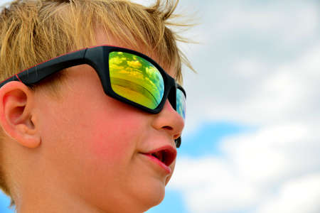 A little boy looks at the cloudy sky with glasses.の写真素材