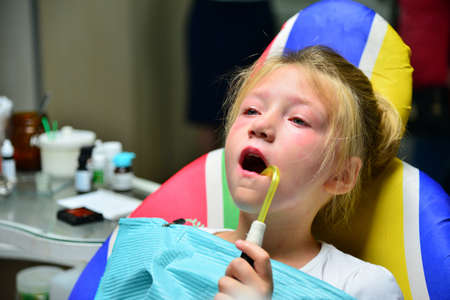 A little girl is curing a tooth at a dentist at a reception sitting on an armchair in the doctor's...