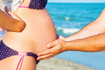 A man is holding a pregnant woman by the stomach on the beachの写真素材