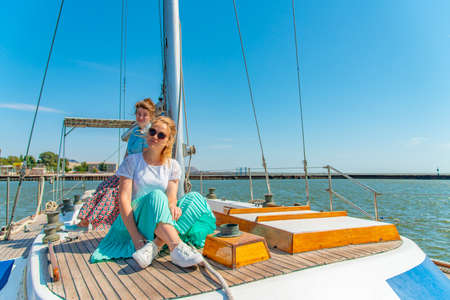 Two girls sit on a yacht on the deck near the mast and look out into the sea