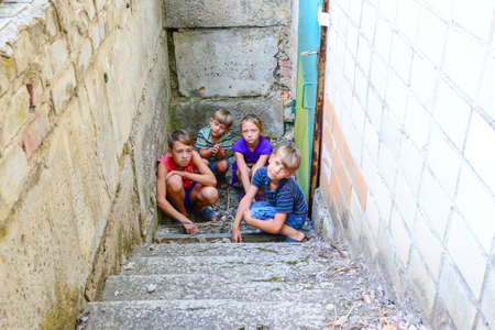 Children in the basement, three boys and a girl near the iron door are hiding on the steps from the outside world. Post-production photo.の写真素材