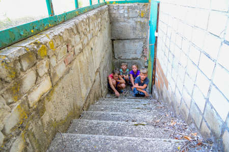 Children in the basement, three boys and a girl near the iron door are hiding on the steps from the outside world. Post-production photo.の写真素材