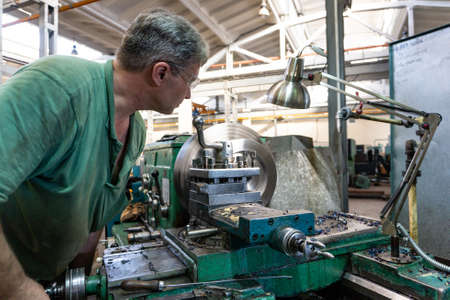 Worker, a man processes metal products on a machine. Turning work in productionの写真素材