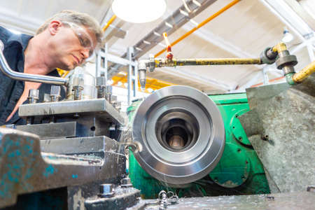 A worker, a man in a black shirt and goggles, controls a mechanical machine. Turning work in...