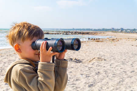 The boy looks through binoculars on the beachの写真素材