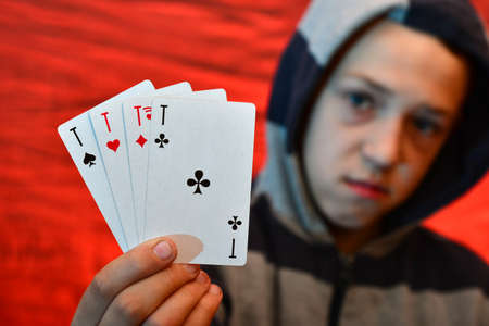 Playing and playing cards in the hands of a man with a hood on a red background.