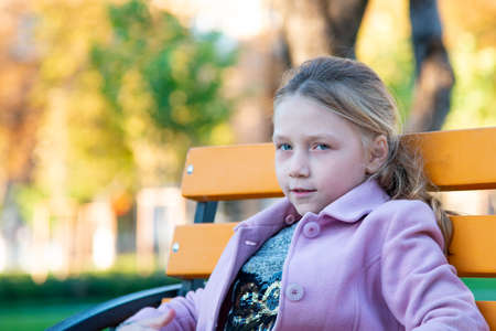 A girl in a pink coat is sitting on a yellow bench in the parkの写真素材