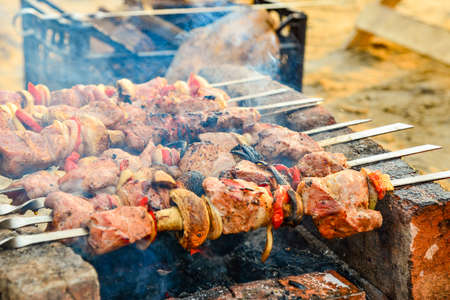 Fried and juicy meat with mushrooms is fried on skewers on a fire, skewers on bricks, under them burning wood coals. Fried meat and mushrooms on the barbecueの写真素材