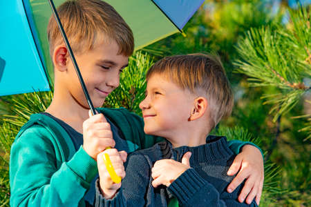 Two brothers stand in an embrace under a bright multi-colored umbrella and look at each other in a...