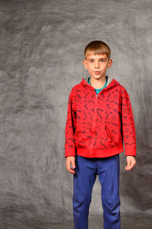 A boy in a red sweater and blue pants is standing in the studio on a gray background