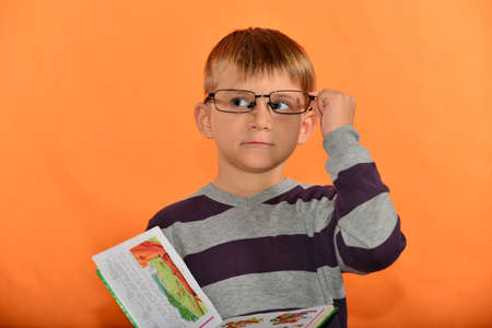 Portrait of a boy in glasses with a book in his hands, cheerful schoolboy on a yellow background...