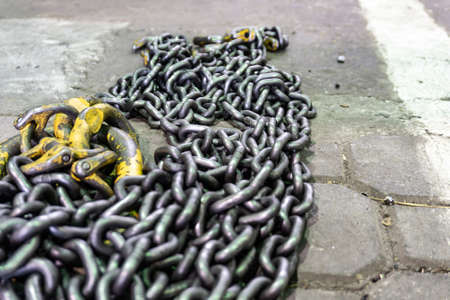 Chains made of iron with hooks of yellow color, for raising a large load, lie on the floor in the production workshop. Abstract industrial backgroundの写真素材