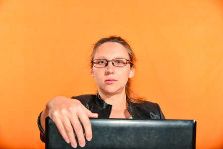 A young girl in a black jacket and glasses holds a laptop and looks into the camera.の写真素材