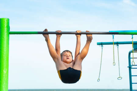 A little boy plays sports on a horizontal bar on the street, performs a workout in athletics.の写真素材
