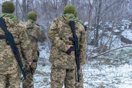 Three soldiers stand in surveillance in the winter in camouflage, holding a machine gun in the rear...