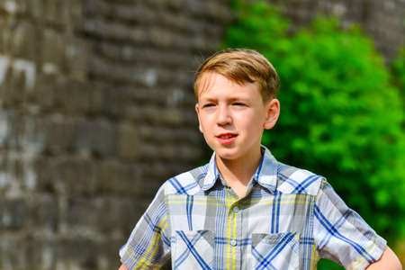 The boy stands thinking on the street against a brick wall.の写真素材