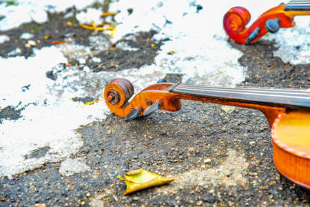 Two violins lie on the asphalt next to the snowの写真素材