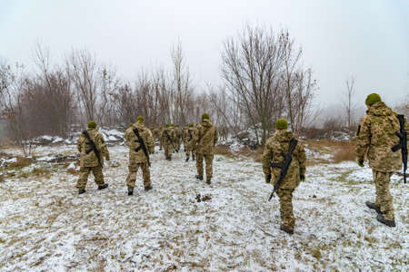 The military in camouflage with Kalashnikov assault rifles, behind their backs, go forward to attack the enemy in winterのeditorial素材