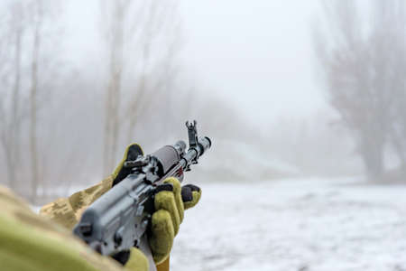 A military soldier takes aim with an automatic rifle and holds it in his mittens in winter.の写真素材