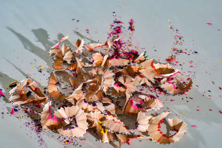 A pile of chips from colored pencils lies on a white table, close-up.