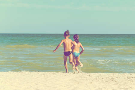 A boy and a girl are running along the beach, a brother and sister are running into the sea.の写真素材