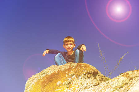 The boy squats on the top of a cliff and looks down.の写真素材
