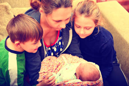 Brother and sister look at the newborn with his mother