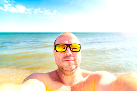 A man in sunglasses makes a selfie at the camera on the beach on vacation.の写真素材