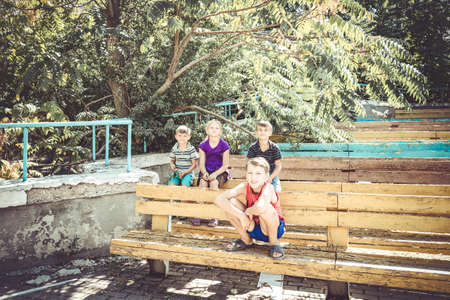 Orphaned children sit in an abandoned park on old benchesの写真素材