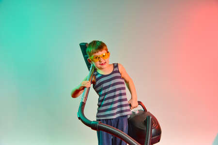 A lovely baby picks up a vacuum cleaner to clean the house.の写真素材