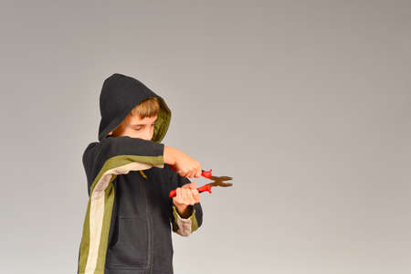 The boy in the hood holds pliers and montage in his hands