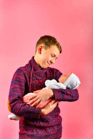 Young dad holds a newborn baby in his arms in the studio on a pink backgroundの写真素材