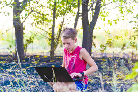 A boy with a laptop in a clearing in the forest is engaged in work and play outdoors in natureの写真素材