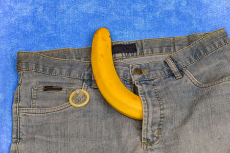 Imitation of an erect penis in jeans with a condom, protruding from the pants in the form of a yellow bananaの写真素材
