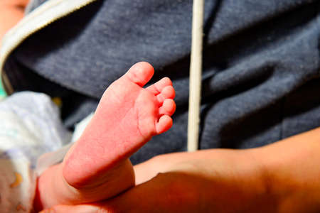 Mom holds in her hand the leg of a newborn baby.