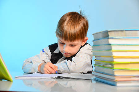 Surprised little schoolboy among notebooks and textbooks at his desk at school in the classroom.の写真素材