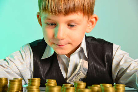 The little boy looks at his cash savings with pleasure. The greedy and vicious concept of the economy of the children's business.の写真素材