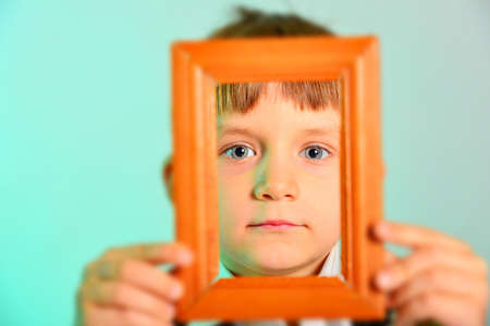 Face framed, boy holds wooden frame near face, close-up.の写真素材