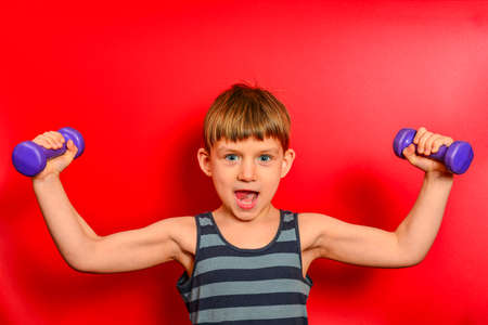 A boy in a striped t-shirt goes in for sports with purple dumbbells on a red background.の写真素材