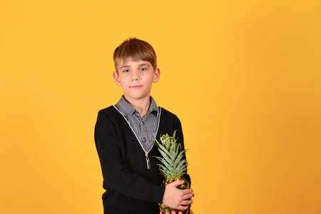 Cute boy pulled pineapple against a yellow background.
