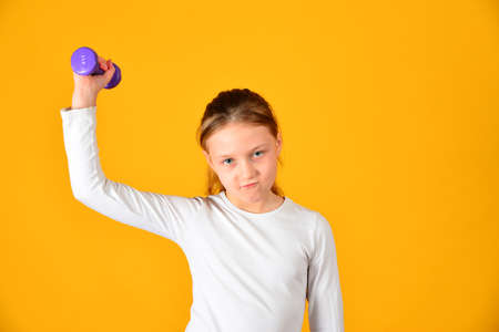 The girl is engaged in fitness with dumbbells, on a yellow background.の写真素材