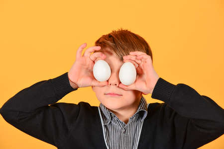 Joyful and cheerful boy holds Easter eggs on his eyes.の写真素材